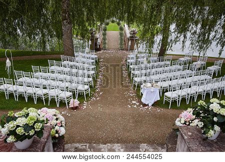 Place For Wedding Ceremony With Wedding Arch Decorated With Flowers And White Chairs On Each Side Of