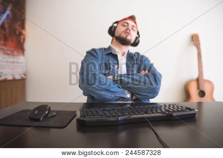 Portrait Of A Gamer With A Beard And A Denim Jacket At A Computer Desk. Focus On The Keyboard And Mo
