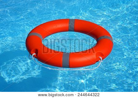 Red Lifebuoy Pool Ring Float On Blue Water. Life Ring Floating On Top Of Sunny Blue Water. Life Ring