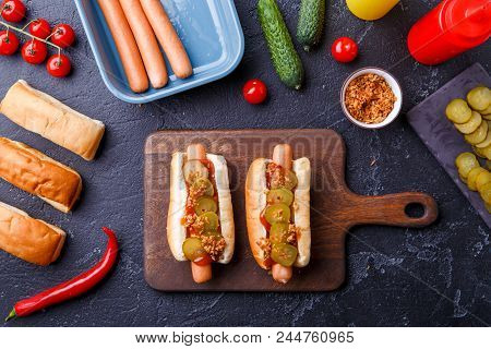 Image On Top Of Two Hotdogs On Cutting Board On Table With Sausages, Bread, Tomatoes
