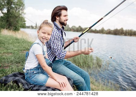 Girl Is Sitting Besides Her Father And Looking At Camera. Guy Is Holding Gish-rod And Fishing. He Is