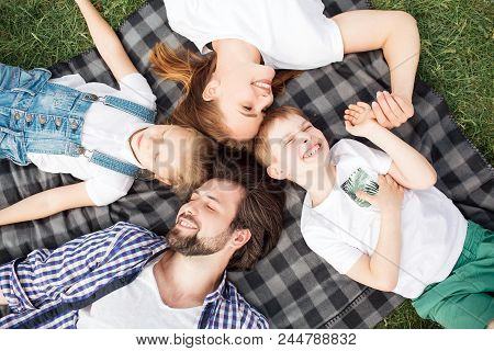 Gorgeous Members Of Family Are Lying On The Blanket On The Grass. Man Is Looking At Daughter. Woman 