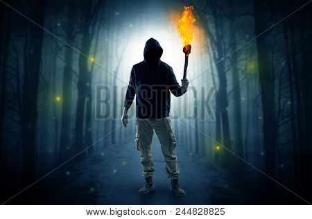Mysterious man coming from a path in the forest with burning flambeau concept