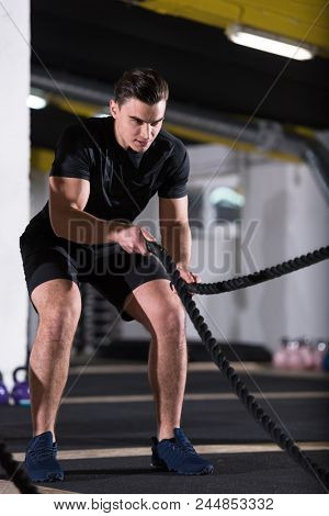young fit athlete man working out in functional training gym doing  battle ropes exercise as part of cross fitness training