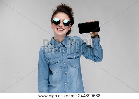 Young Girl In Round Glasses On A Gray Background. Portrait Of A Young Beautiful Girl. Charming Girl 