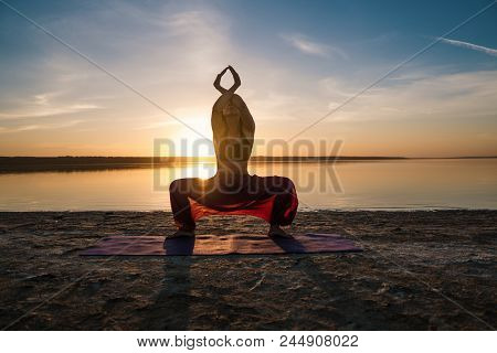 Woman On The Beach At Sunset Starts Doing Yoga Asana Training . Morning Natural Stretch Warm-up Trai