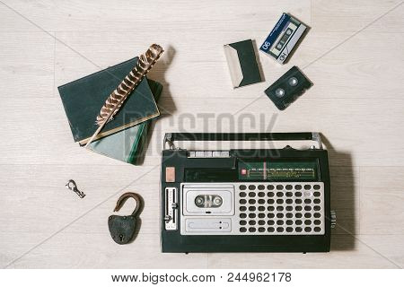 Old Cassette Tape Recorder, Key, Lock, Books And Feather On Wooden White Background. Top View. Layfl