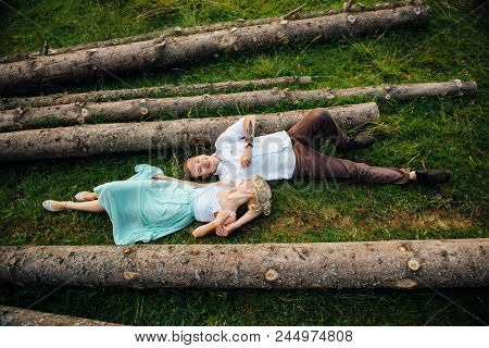 Couple In Love Walking Near Logs In The Mountains.