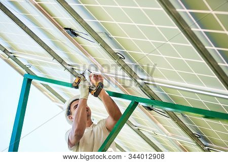 Mounter Installing Solar Panel On Metallic Carcass Using Drill. Cropped Photo Of Man Standing On Lad