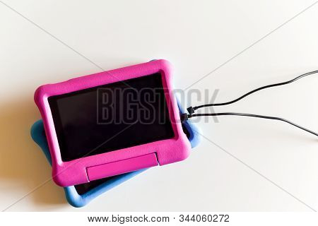 Two kids tablet devices to play games and educational apps plugged in to power supply cable