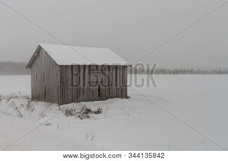 An Old Abandoned Barn House Stands On The Snowy Fields At The Rural Finland. The Snow Storm Is Cover