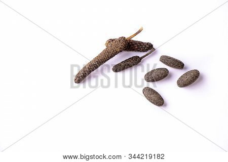 Dry Long Pepper Fruits And Brown Ayurvedic Tablets Scattered On White Background. Herbal Medicine Co