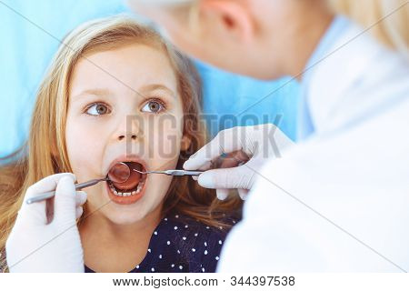 Little Baby Girl Sitting At Dental Chair With Open Mouth During Oral Check Up While Doctor. Visiting