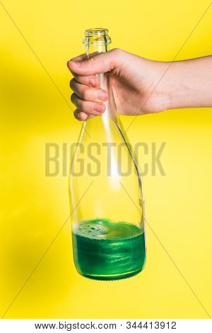 An Open Bottle Of Champagne Is Half Empty On A Yellow Background. Mans Hand Holds A Bottle With Alco