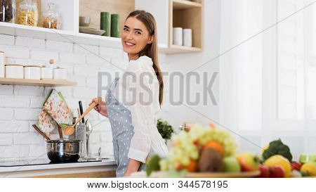 Cooking Lunch. Young Woman Preparing Meal On Stove, Stiring Soup And Smiling To Camera, Panorama Wit
