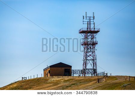 A Wide Angle View Of A Steel Lattice Cellular Base Station Tower By A Small Brick Building Atop A Hi