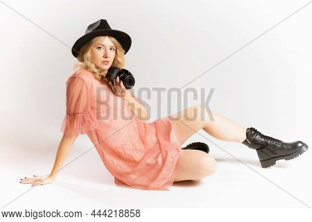 Portrait Of A Cute Girl Photographer In A Hat Posing With A Camera In Her Hands In The Studio On A W