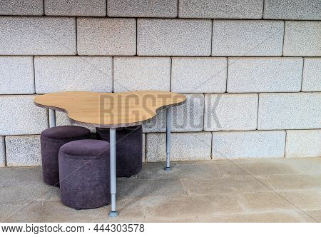 Table And Three Stools Against Exterior Wall Of Building In Public Park.