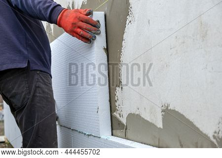 Construction Worker Installing Styrofoam Insulation Sheets On House Facade Wall For Thermal Protecti