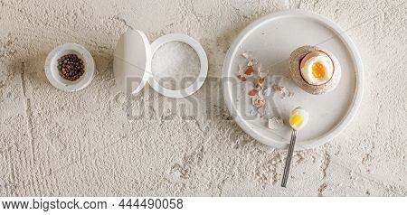 One Boiled Egg In Stoneware Egg Cup With Egg Shell Broken Pieces In Concrete Tray, Salt Flakes And P