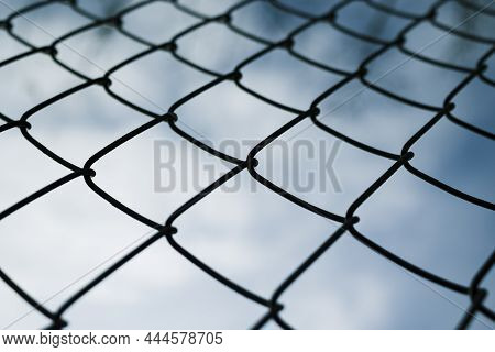 Dramaic Blue Sky With White Clouds Through A Metal Grid Chain Fence . Low Angle View