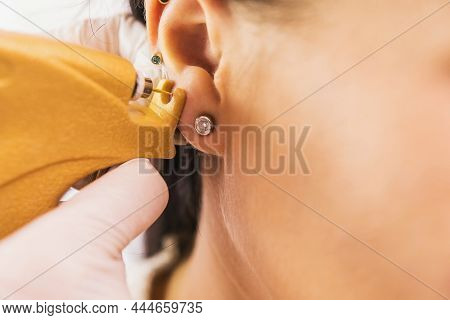 A Doctor In Sterile White Medical Gloves Pierces The Ears Of A Young Girl In The Medical Office With