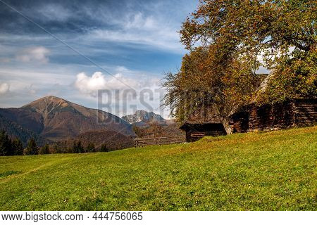 Wooden Cottage On Meadow And Mountains At Background. Village Podsip At Slovakia.