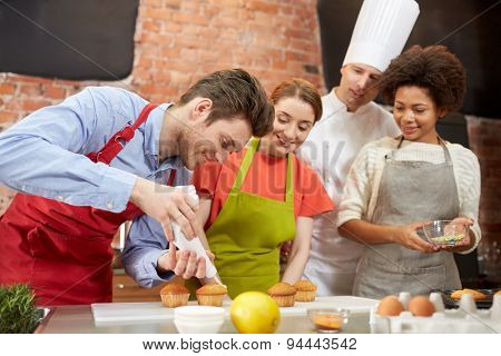 cooking class, culinary, bakery, food and people concept - happy group of friends and male chef cook baking in kitchen