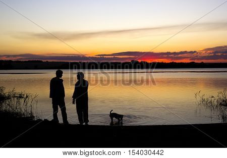 two men are talking and dog is walking