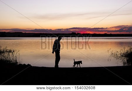 boy is playing with dog at lake during sunset