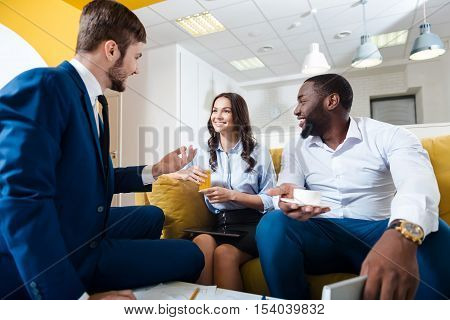Rapid lifestyle. Joyful delighted colleagues talking and discussing project while sitting in the office