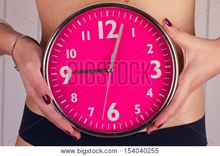 Biological clock ticking . Pink clock in female hands. toning