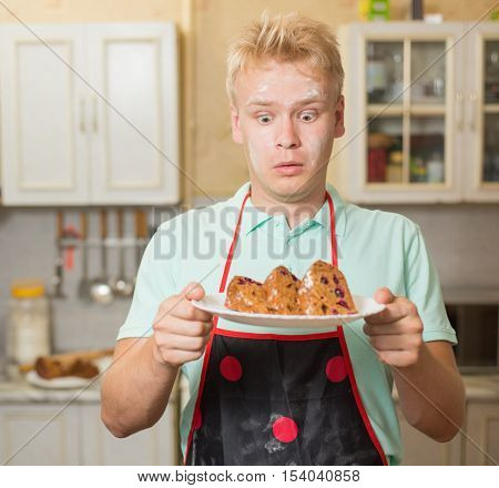 Surprised young man with flour on his face holding cupcake.