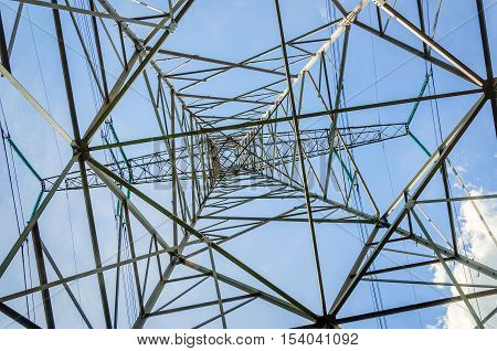 Construction of a steel high-voltage pylon against a blue sky as seen from below. It is a sunny day in the summer season.