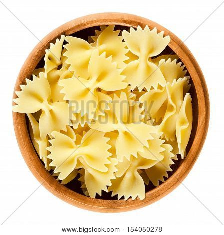 Farfalle pasta in wooden bowl. Uncooked dried durum wheat semolina pasta. Decorative short-cut bow tie or butterfly shaped Italian noodles. Isolated macro food photo over white background.