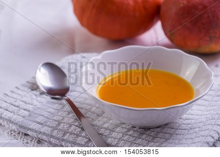 Pumpkin hokkaido soup on white tablecloth with two pumpkins behind.