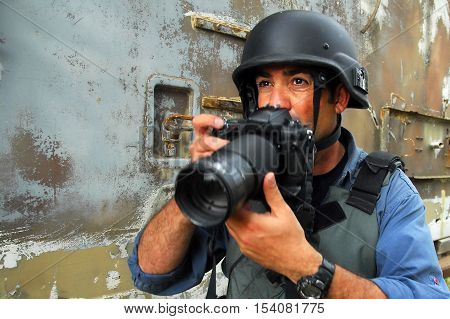 Photojournalist wearing protective clothing including a hard hat and vest documenting war and conflict.