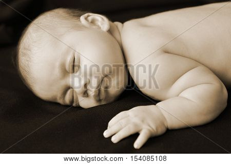 A newborn baby sleeps on a black blanket in peace.