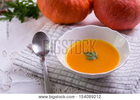 Pumpkin hokkaido soup on white tablecloth with two pumpkins behind.