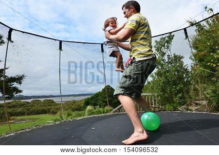 Father and his baby jumping together on a trampoline.