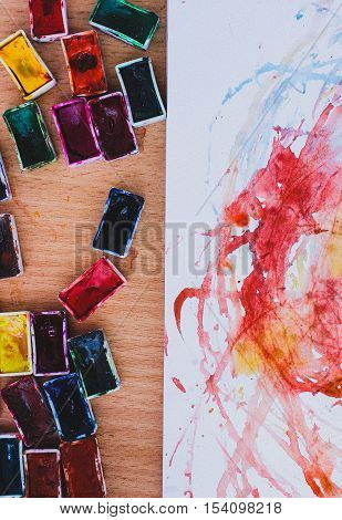 Top view of watercolor containers and album with abstract preschooler's drawings.