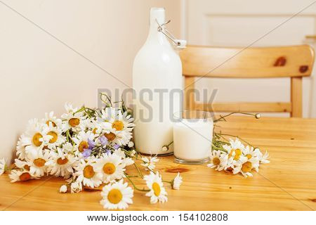 Simply stylish wooden kitchen with bottle of milk and glass on table, summer flowers camomile, healthy foog moring concept noone