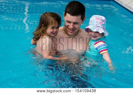 Father and his two daughter baby girls in the pool during summer vacation.