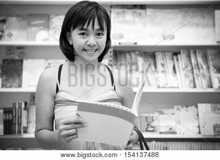 middle age attractive mature Asian woman with book in hands with blurry booshelf background - model looking at camera black and white style