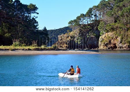 Couple rows a rubber inflatable dinghy boat to Roberton Island in the Bay of Islands New Zealand.