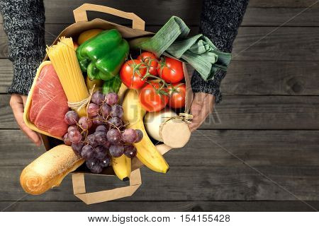 Man holding brown paper bag full of different healthy food on a wooden table top view