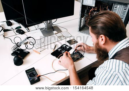 Programmer testing circuit with multimeter. Electronic repairman examine inside parts of CPU in repair shop