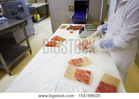 Worker puts pieces of red saltfish on foiled paper into packages at fish factory.