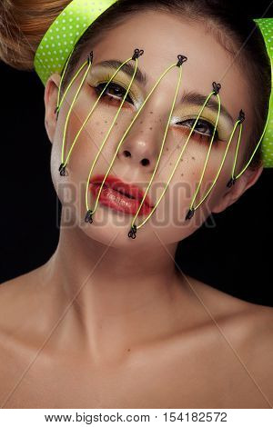 Woman in conceptual make up with neon thread on face on black background in studio photo. Extreme beauty fashion make up