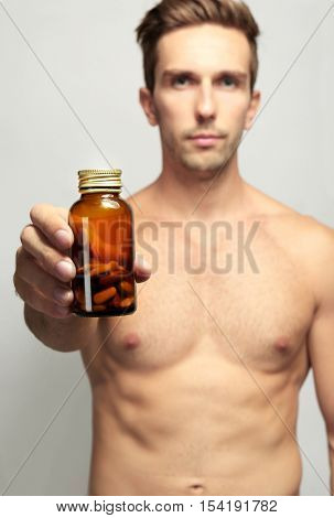 Muscular man holding drugs in bottle, closeup